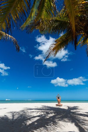 Foto de Hermosa joven meditando en una playa de Progreso México durante el día soleado. Playa blanca con palmeras y cielo azul. - Imagen libre de derechos