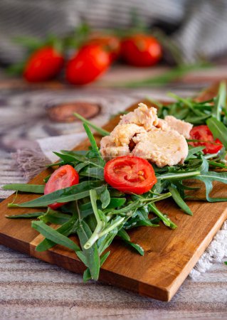 Light appetizer with rocket, tuna and red cherry tomatoes on a wooden cutting board