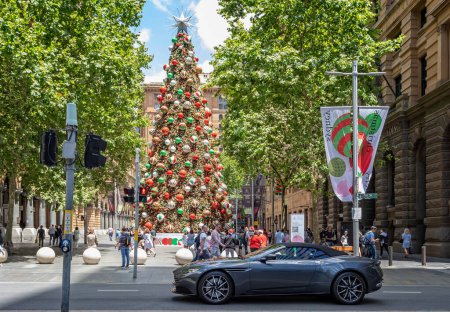 Téléchargez les photos : Nouvelle voiture de sport gris métallisé foncé Aston Martin devant un immense sapin de Noël décoré dans le centre de Sydney, en Australie, le 9 décembre 2022 - en image libre de droit
