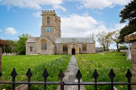 Photo for Pathway lined with yellow buttercups and daffodils leading to the Church of St Mary in the village of Burton Bradstock, Dorset, UK on 5 May 2023 - Royalty Free Image