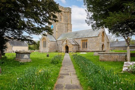 Photo for Pathway lined with yellow buttercups and daffodils leading to the Church of St Mary in the village of Burton Bradstock, Dorset, UK on 5 May 2023 - Royalty Free Image