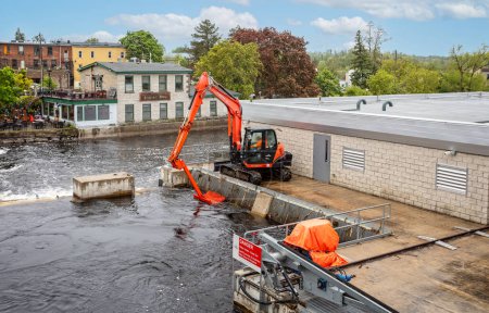 Téléchargez les photos : Drageuse nettoyant les débris de la prise d'eau à la génératrice hydroélectrique à Almonte, Ontario, Canada le 24 mai 2023 - en image libre de droit