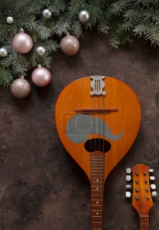 Photo for Old mandolin and fir-tree branches with Christmas decor. Christmas and New Year's concept. Top view, close-up on dark brown background - Royalty Free Image