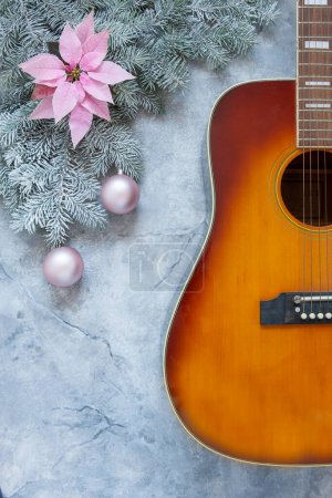 Photo for Acoustic guitar and snow fir tree branches with gentle poinsettia flower and  Christmas balls on light marble background. - Royalty Free Image