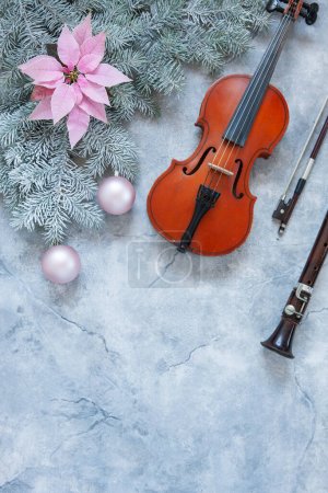 Photo for Old violin and flute with fir-tree branches with gentle pink poinsettia flower and Christmas decor. Christmas and New Year's concept. Top view, close-up on dark concrete background. - Royalty Free Image