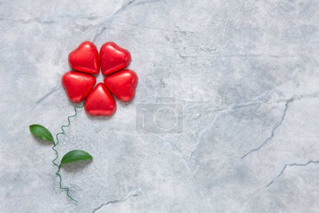 Foto de Primer plano de chocolates en forma de corazón en envoltura roja, doblados en flor. Fondo, vista superior, espacio para copiar - Imagen libre de derechos