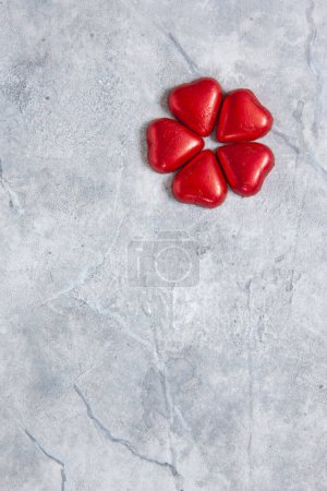 Foto de Primer plano de chocolates en forma de corazón en envoltura roja, doblados en flor. Fondo, vista superior, espacio para copiar - Imagen libre de derechos