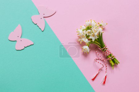 Photo for Fresh beautiful bouquet of the first spring forest snowdrops with a red and white martisor cord and a butterfly figure - a traditional symbol of the first spring day on a pink pastel and green paper background - Royalty Free Image