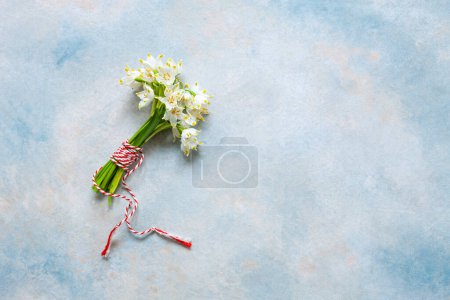 Photo for Fresh beautiful bouquet of the first spring forest snowdrops flowers with red and white cord martisor - traditional symbol of the first spring day on sky blue background - Royalty Free Image
