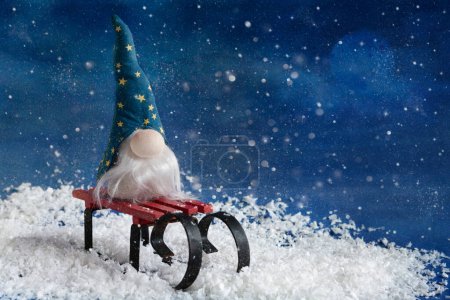 Foto de Christmas gnome Gonk wearing blue hat with long beard sits on the sledges. New year and Christmas greeting card design. - Imagen libre de derechos