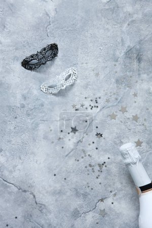 Photo for White and Black   Carnival masks, white champagne bottle and silver glitter confetti. Top view, Close up on marble background. - Royalty Free Image