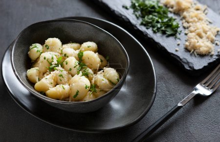 Téléchargez les photos : Traditional homemade cooked italian potato gnocchi with butter, parsley and parmesan cheese on dark gray background - en image libre de droit
