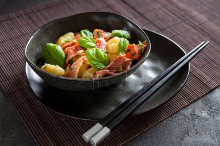 Foto de Traditional homemade cooked italian potato gnocchi baked with bacon, parsley served with chopstick on dark gray background - Imagen libre de derechos
