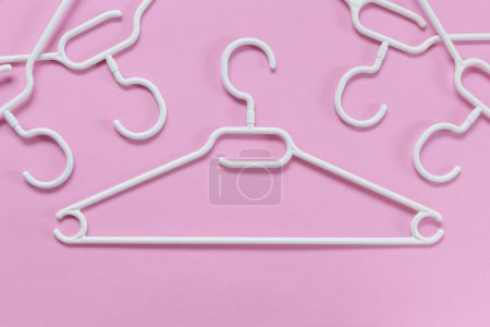 Téléchargez les photos : Cintres en plastique blanc sur fond rose. Concept vente, boutique, occasion, commerce en ligne, plateforme de revente de marque - en image libre de droit
