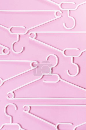 Téléchargez les photos : Cintres en plastique blanc sur fond rose. Concept vente, boutique, occasion, commerce en ligne, plateforme de revente de marque - en image libre de droit