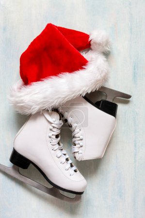 Photo for White figure skates and red Santa hat on the blue light background - Royalty Free Image