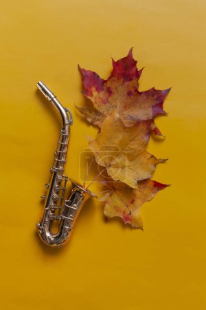Photo for Miniature golden saxophone copy on the yellow autumn maple leaves background. Top view, close-up. - Royalty Free Image