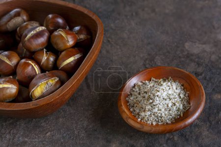 Photo for Fresh sweet baked edible chestnuts in wooden bowl with rosemarin sea salt, closeup - Royalty Free Image