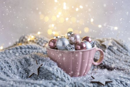 Foto de Bolas de Navidad de plata y rosa en la taza grande de color rosa, bufanda de punto gris de cerca en el fondo nevado y bokeh - Imagen libre de derechos