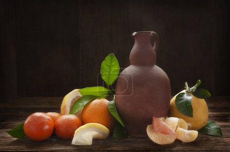 Foto de Naranjas, mandarinas, limones y jarra de cerámica vintage sobre una antigua mesa de madera. Bodegón artístico en estilo vintage. - Imagen libre de derechos
