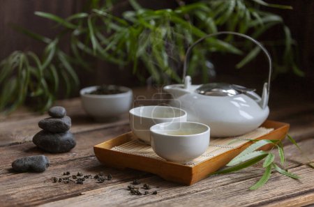 Foto de Conjunto tradicional de ceremonia del té verde - tetera blanca y tazas con piedras piramida, casa para el alma, en el tra - Imagen libre de derechos