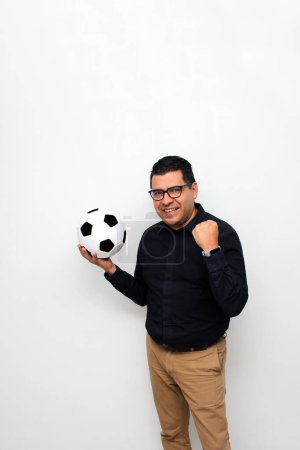 Foto de Hombre de oficina adulto latino juega con una pelota de fútbol muy emocionado de que va a ver el juego y quiere ver a su equipo ganar - Imagen libre de derechos