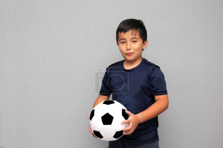Photo for Hispanic Latino 8-year-old boy plays with a soccer ball very excited that he is going to see the football game and wants to see his team win - Royalty Free Image