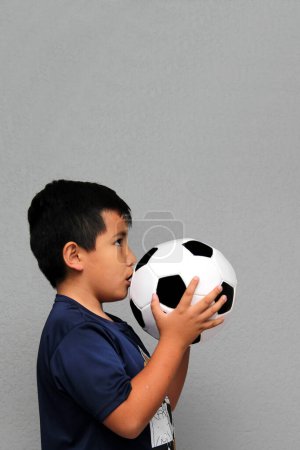 Photo for Hispanic Latino 8-year-old boy plays with a soccer ball very excited that he is going to see the football game and wants to see his team win - Royalty Free Image