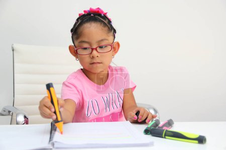 Foto de 4-year-old brunette Latina girl with autism spectrum disorder ASD like Asperger, Rett and Heller draws at a desk, plays with colors alone antisocial - Imagen libre de derechos