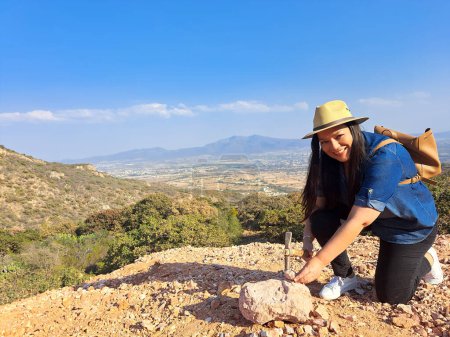 Photo for Latina woman with hat and miner's pick hammer works as a geologist, studies the composition and structure of the mineral soil of the mountain - Royalty Free Image