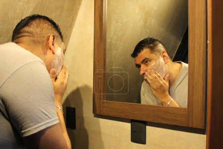 Photo for Dark-haired 40-year-old Latino man does his beauty routine, shaves with shaving cream and soap to avoid folliculitis - Royalty Free Image