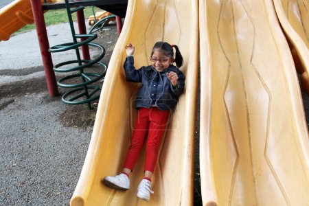 Photo for 4-year-old brunette Latina girl plays on the slide in the park living in poverty and happy - Royalty Free Image