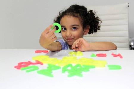 Foto de Morena latina de 3 años juega con letras y números de juguete para mejorar su idioma, aprender a leer y escribir - Imagen libre de derechos