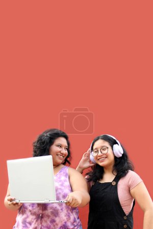 Téléchargez les photos : Deux jeunes femmes brunes latines de 20 ans utilisent un ordinateur portable et des écouteurs pour étudier et se divertir en regardant des vidéos musicales - en image libre de droit