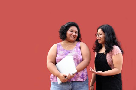 Téléchargez les photos : Deux jeunes femmes brunes latines de 20 ans utilisent un ordinateur portable et des écouteurs pour étudier et se divertir en regardant des vidéos musicales - en image libre de droit
