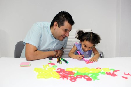 Téléchargez les photos : Divorcé père célibataire avec sa fille brune Latino cheveux bouclés faire des devoirs, jouer, s'amuser et passer du temps de qualité - en image libre de droit