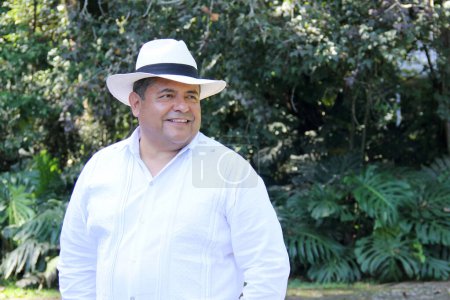Dark-skinned Latino 50 year old man dressed in guayabera and hat, traditional Latin American dress, enjoys a walk outdoors