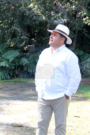 Dark-skinned Latino 50 year old man dressed in guayabera and hat, traditional Latin American dress, enjoys a walk outdoors