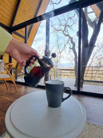 Kaffeezubereitung in einer französischen Presse oder Kaffeemaschine in einer Hütte inmitten des Waldes als Symbol für Entspannung und Luxus