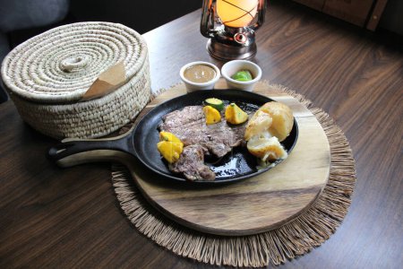 Carne asada acompañada de pimientos y papas al horno con tortillas, frijoles y limones al estilo mexicano
