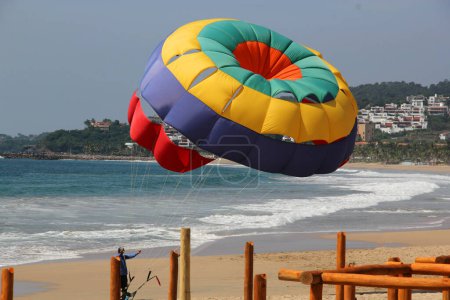 Photo for Parasailing, Parascending or Parakiting is an aquatic activity where a person attached to a parachute is towed by a boat at speed, causing them to rise above the water - Royalty Free Image