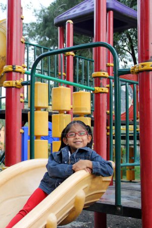 Chica morena latina de 4 años con anteojos juega en los juegos del parque en la soledad y la pobreza pasa sus días de vacaciones con autismo