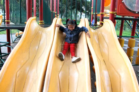 Foto de Chica morena latina de 4 años con anteojos juega en los juegos del parque en la soledad y la pobreza pasa sus días de vacaciones con autismo - Imagen libre de derechos