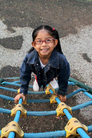 Foto de Chica morena latina de 4 años con anteojos juega en los juegos del parque en la soledad y la pobreza pasa sus días de vacaciones con autismo - Imagen libre de derechos