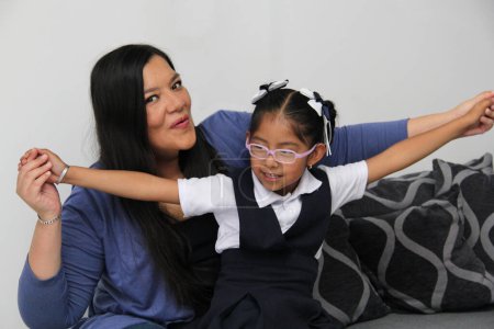 Geschiedene alleinerziehende lateinamerikanische Mutter und brünette 4-jährige Tochter in Uniform und Brille reden und spielen nach der Schule