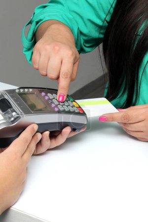 Eine erwachsene Frau mit Kaffee in der Hand bezahlt mit einer kontaktlosen Kreditkarte in einem Geschäft und gibt ihre PIN ein