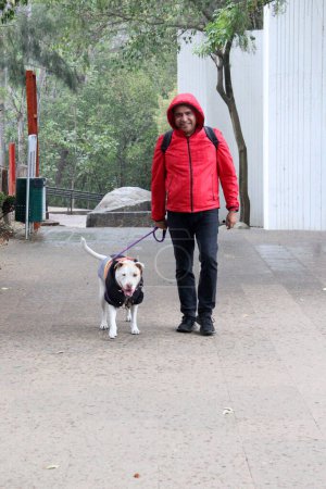 Divorciado hombre soltero de 40 años latino de piel oscura se prepara para caminar bajo la lluvia en el parque con su perro de apoyo emocional