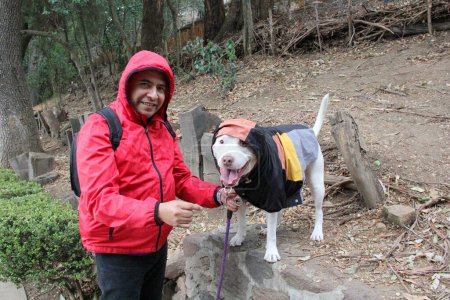 Divorciado hombre soltero de 40 años latino de piel oscura se prepara para caminar bajo la lluvia en el parque con su perro de apoyo emocional