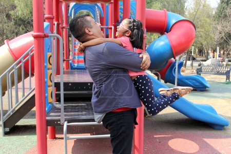 Divorced single dad plays with his brunette latina daughter in playground park spins and hugs spend fun time