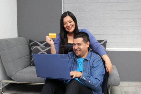 Couple of 40 year old Latino man and woman use their laptop and credit card to shop online excited about discounts and promotions